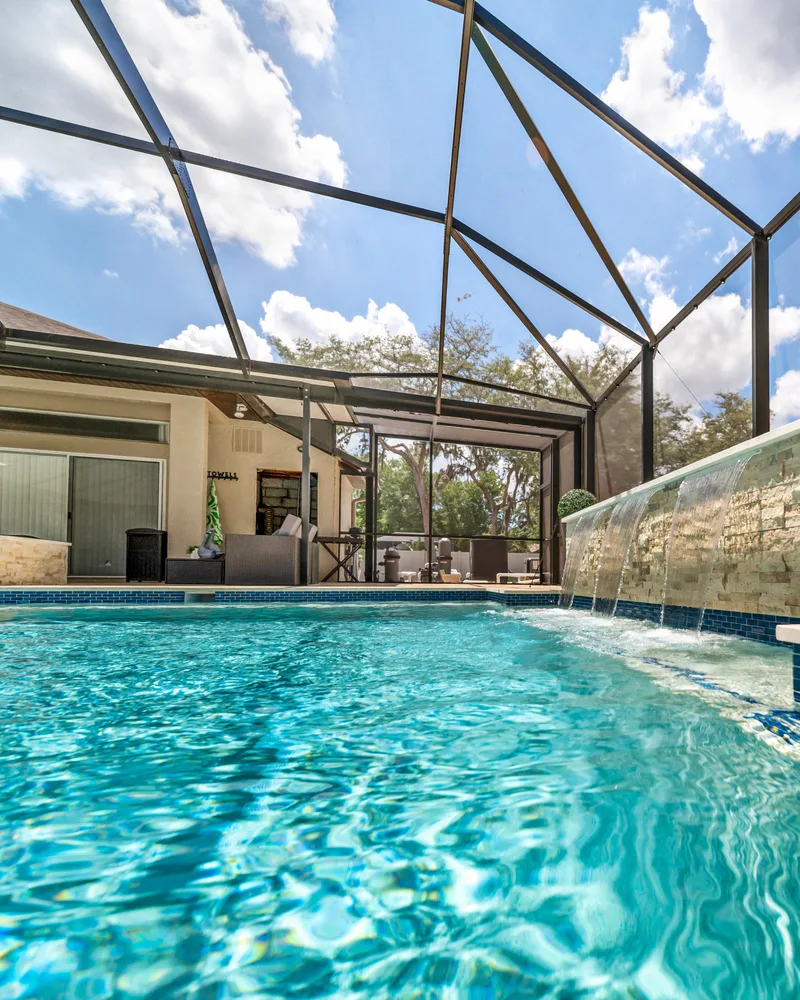 Custom pool with a stacked stone water wall and ivory travertine decking built by Pool Perfection in Odessa