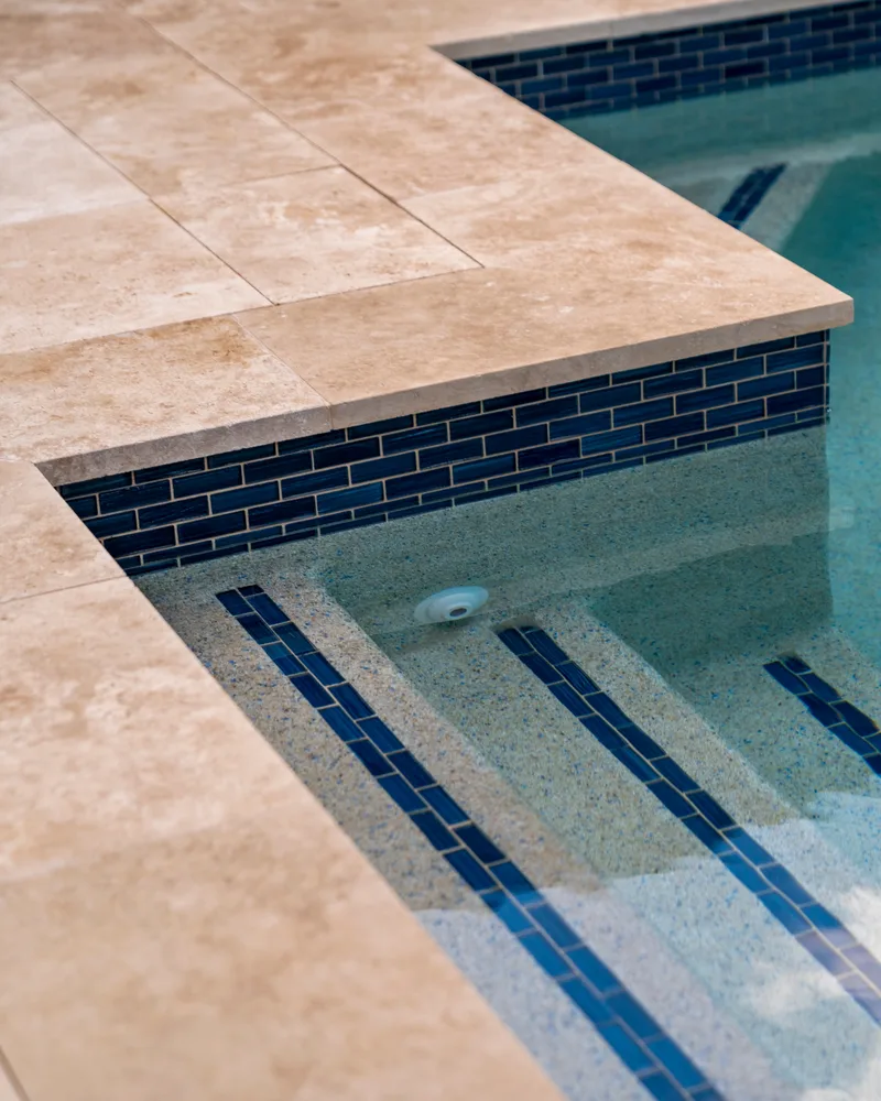 Ivory travertine coping and decking meeting blue Cayman waterline tile